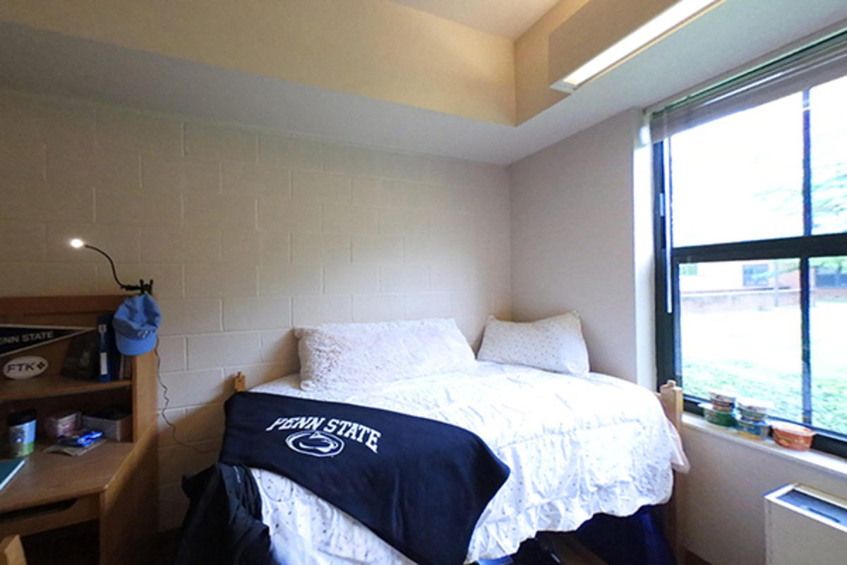 A tidy dorm room with a neatly made bed featuring a Penn State blanket.