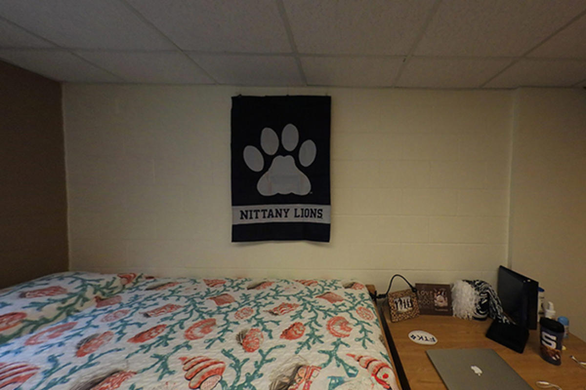A Nittany Lions banner hangs above a bed in a dorm room.
