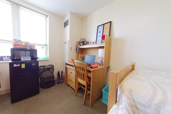 A neatly organized dorm room with a bed, furniture, appliances, and personal items.