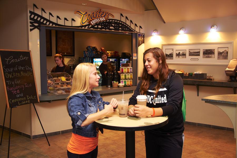 Two students enjoying beverages at a table near Coasters Coffee Shop