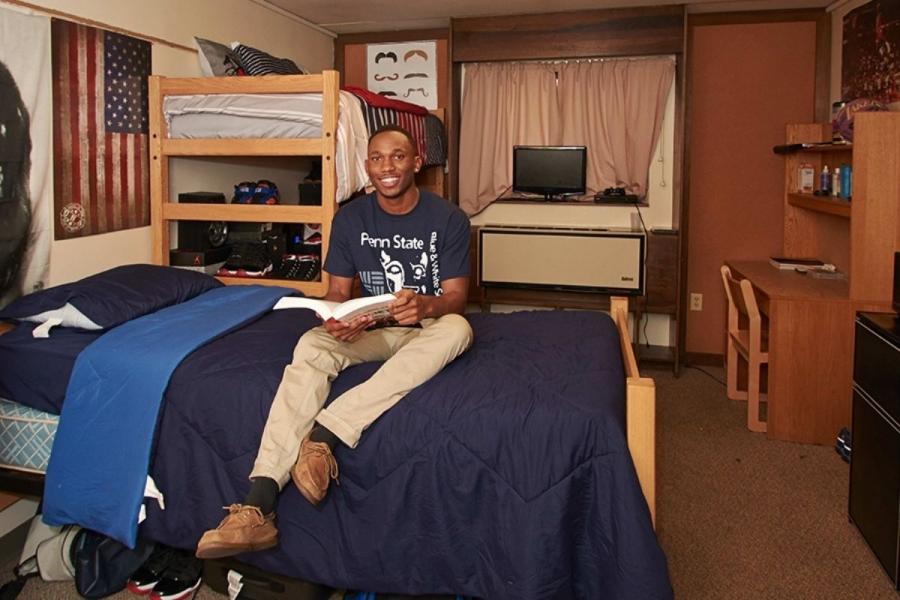 Male student sitting on bed in residence hall room