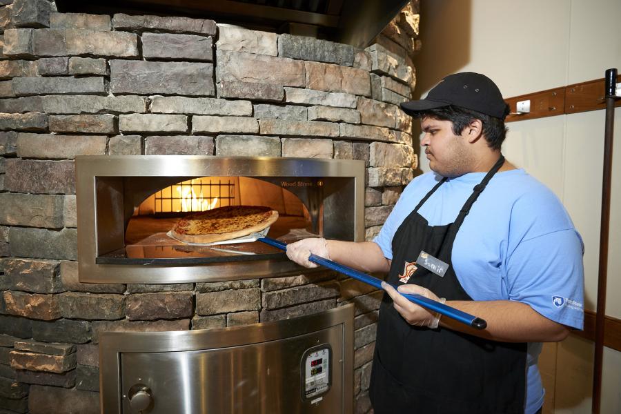 Student employee getting pizza out of the brick pizza oven