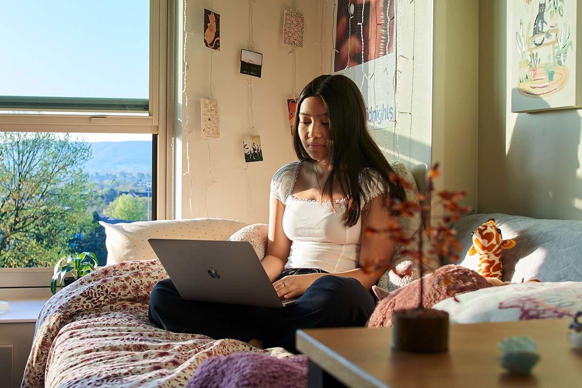 college student sitting on bed in residence hall room