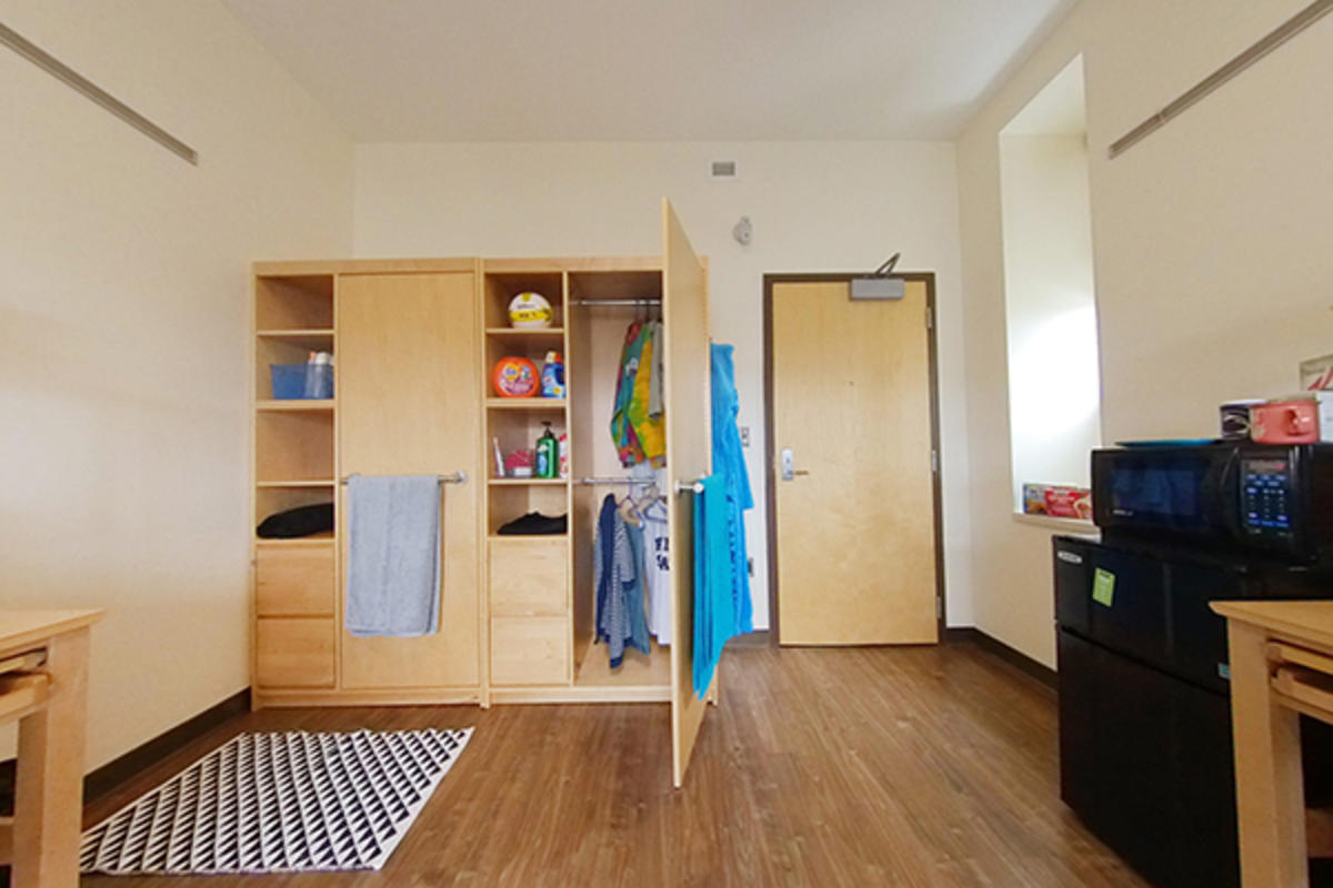 A well-organized dorm room with wooden furniture and storage.