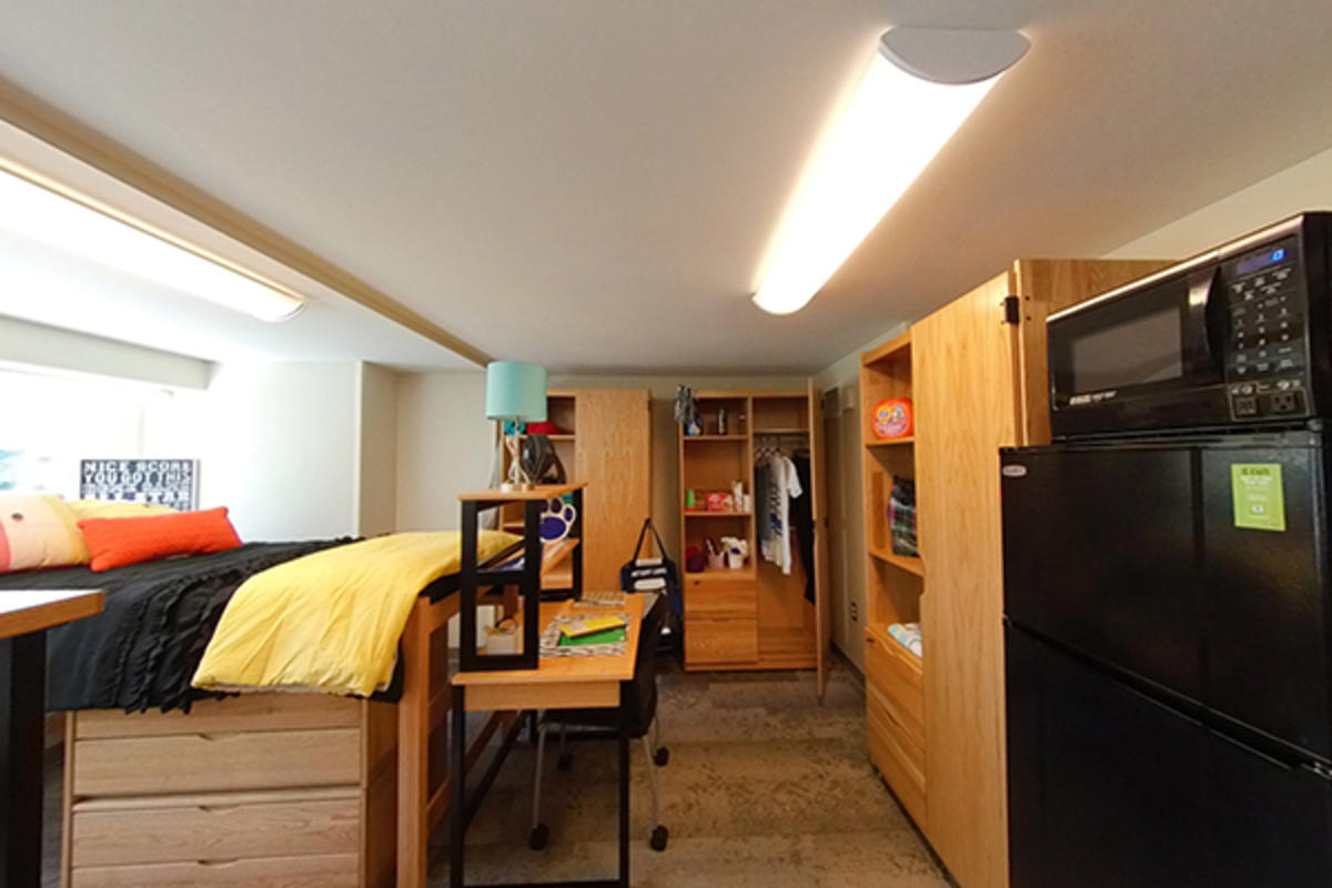 A well-organized dorm room with wooden furniture, storage, and appliances.