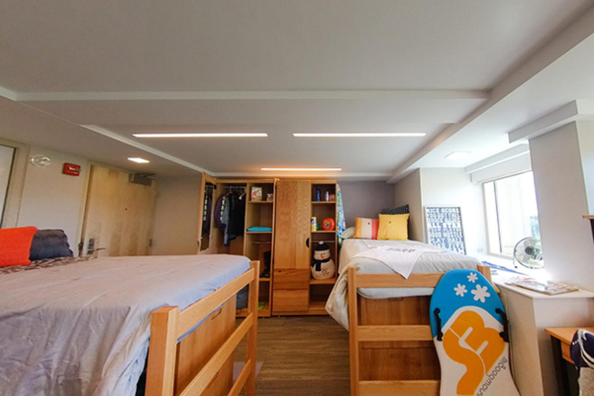A well-organized dorm room with two beds, modern lighting, and storage.