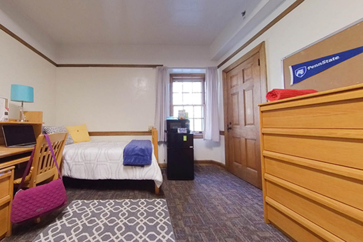 A neatly organized dorm room with a bed, furniture, appliances, and personal items.