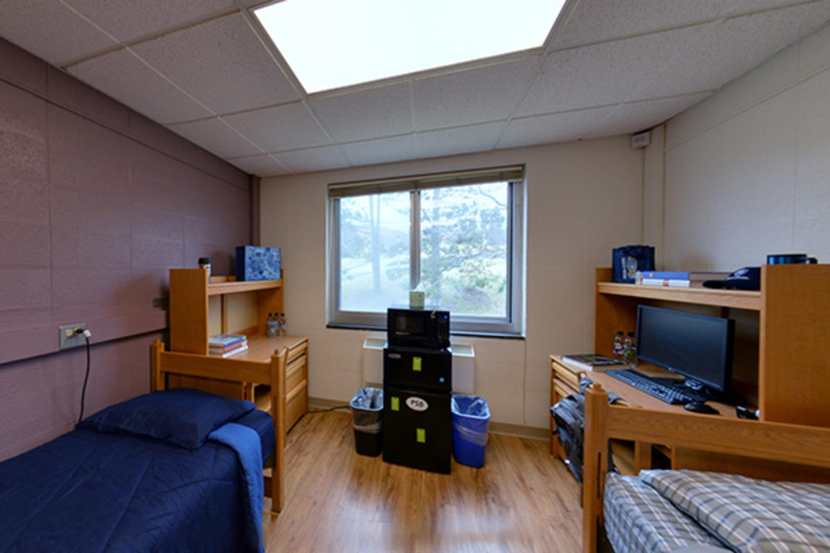 A tidy dorm room with two beds, desks, and shelving units.