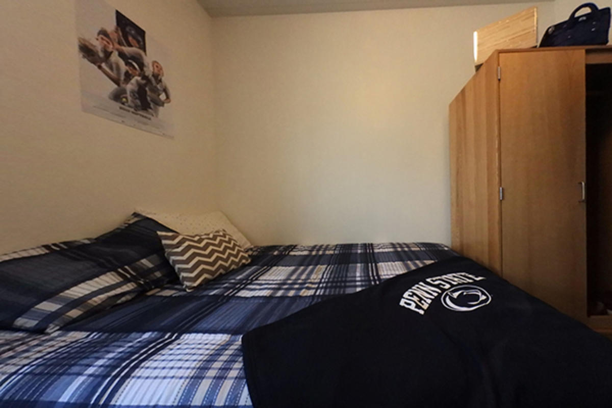 A tidy dorm room with a neatly made bed featuring a Penn State blanket.