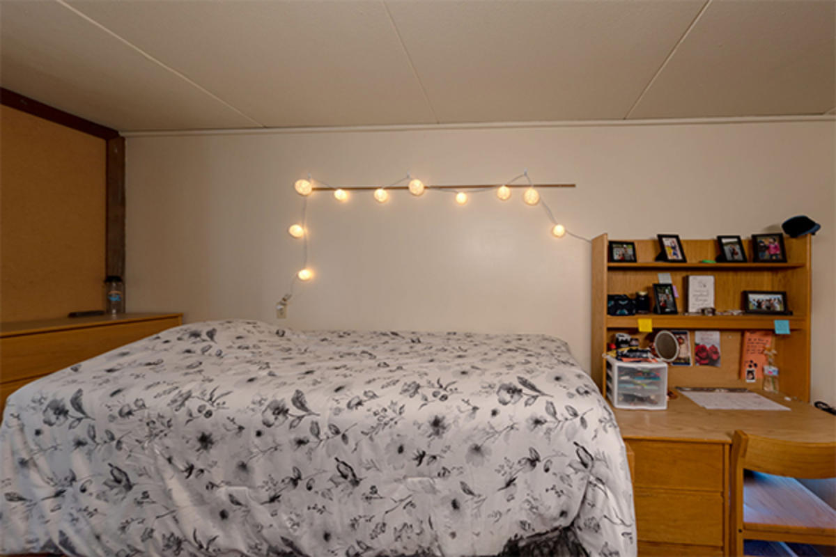 A tidy dorm room with a bed and wooden furniture.