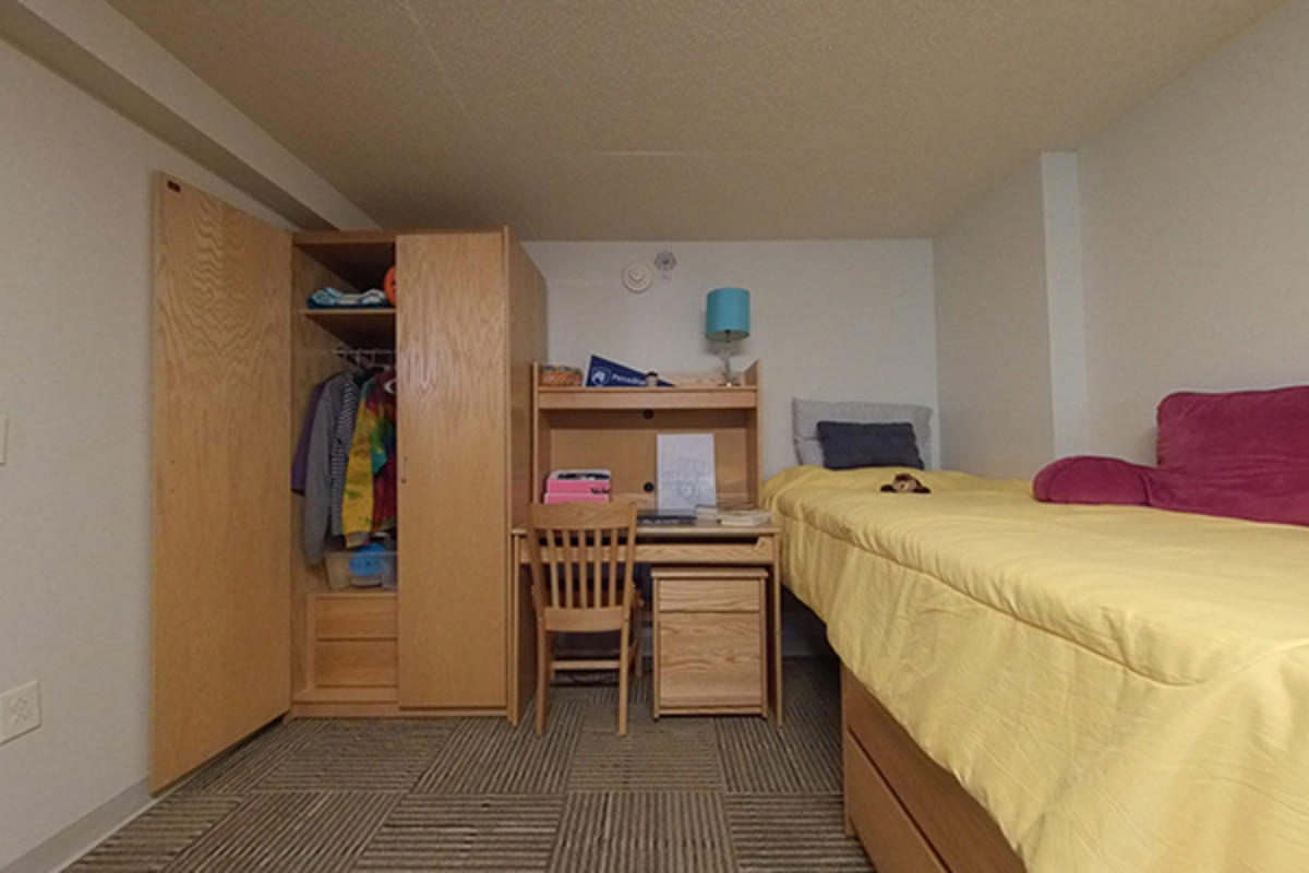 A well-organized dorm room with wooden furniture, storage, and a bed.