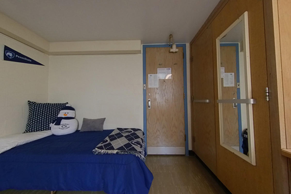 A tidy dorm room with a neatly made bed featuring a Nittany Lion blanket.