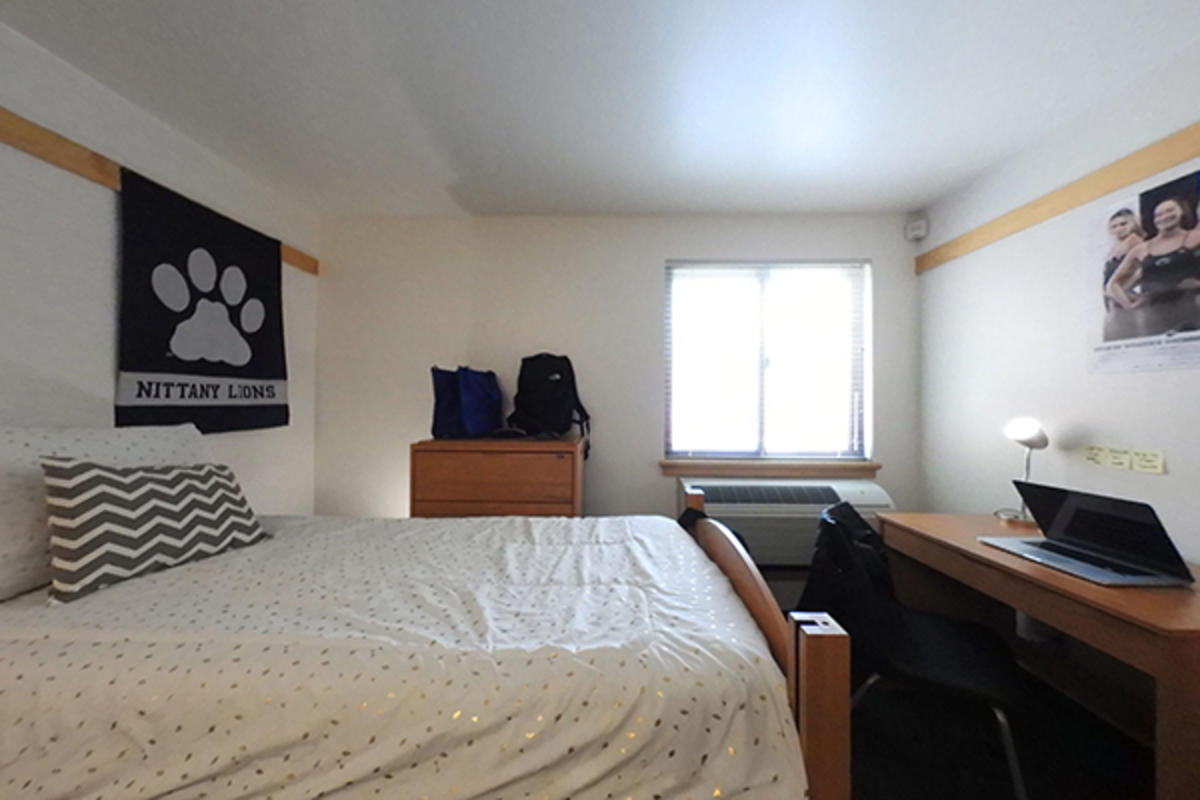 A well-organized college dorm room with a made bed, Nittany Lions banner, and study desk.