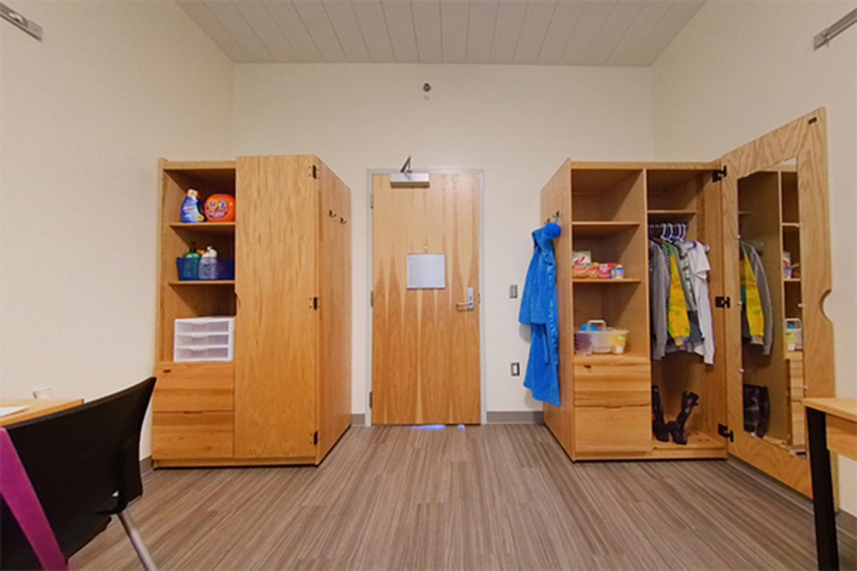 A tidy dorm room with desks, wooden furniture, and storage.