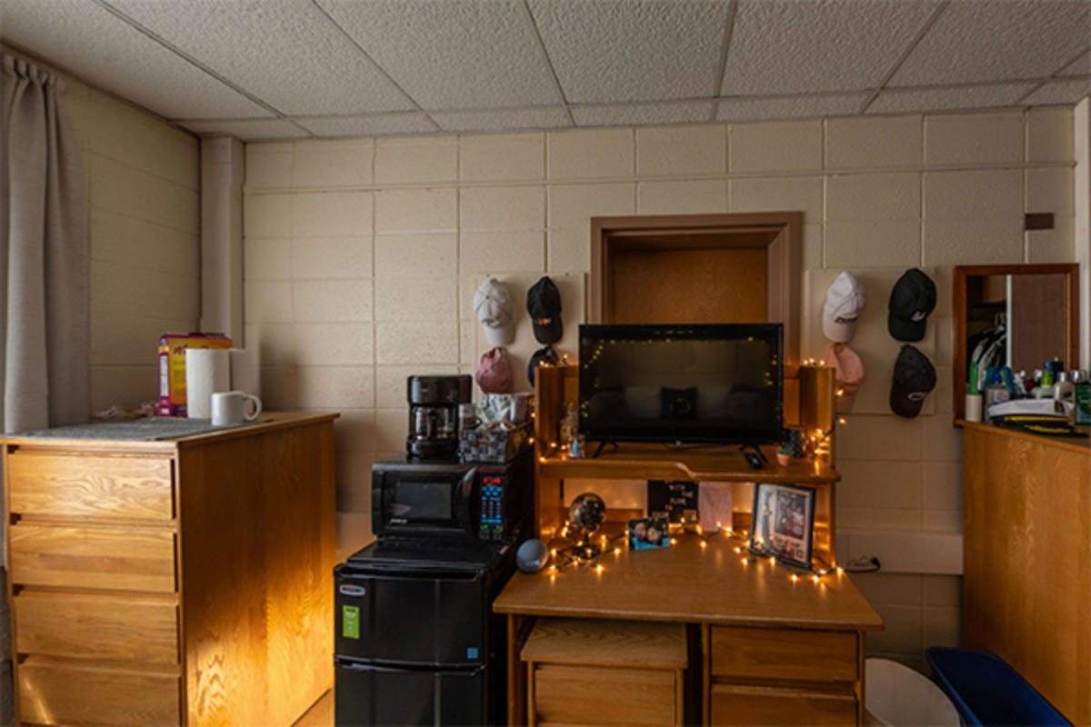A neatly organized dorm room with furniture, appliances, and personal items.