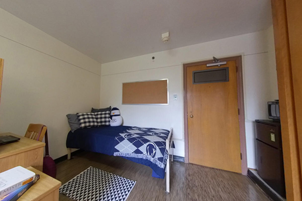 A neatly organized dorm room with a bed, furniture, appliances, and a desk.