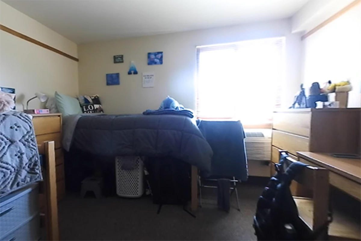 A tidy dorm room with a bed and wooden furniture.