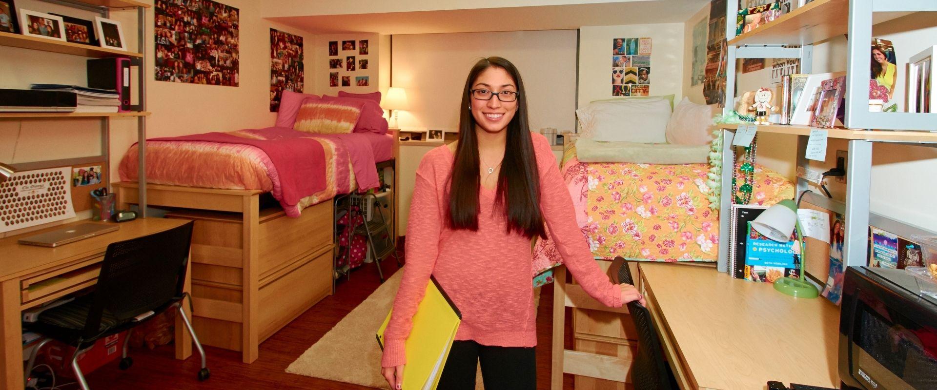 female student standing in front of beds in residence hall