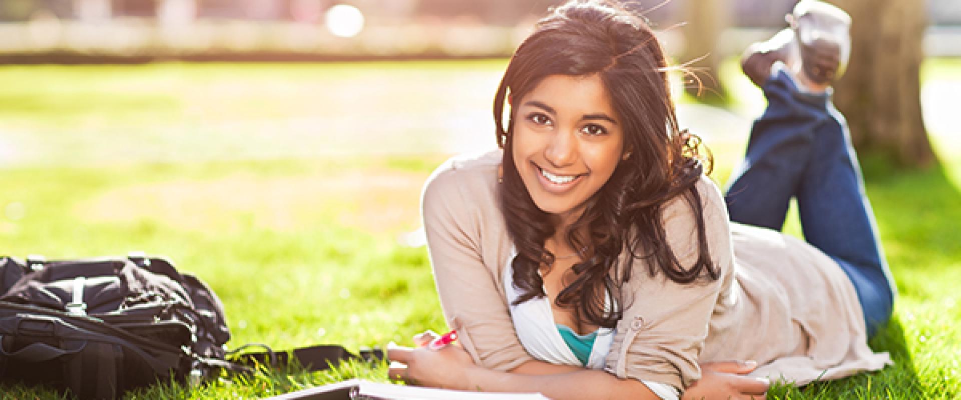 student laying on grass studying