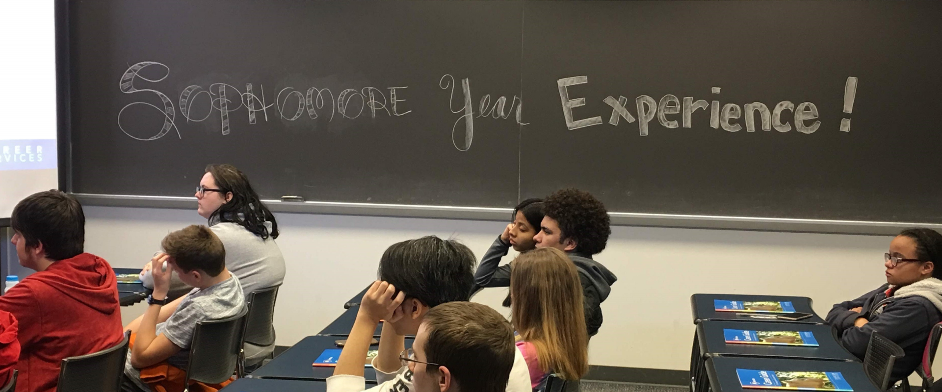students sitting in classroom; "Sophomore Year Experience" handwritten on chalkboard