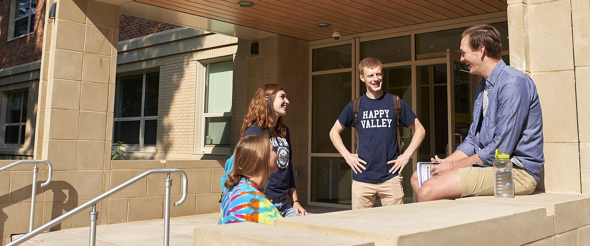 Students sitting outside of a residence hall talking and laughing