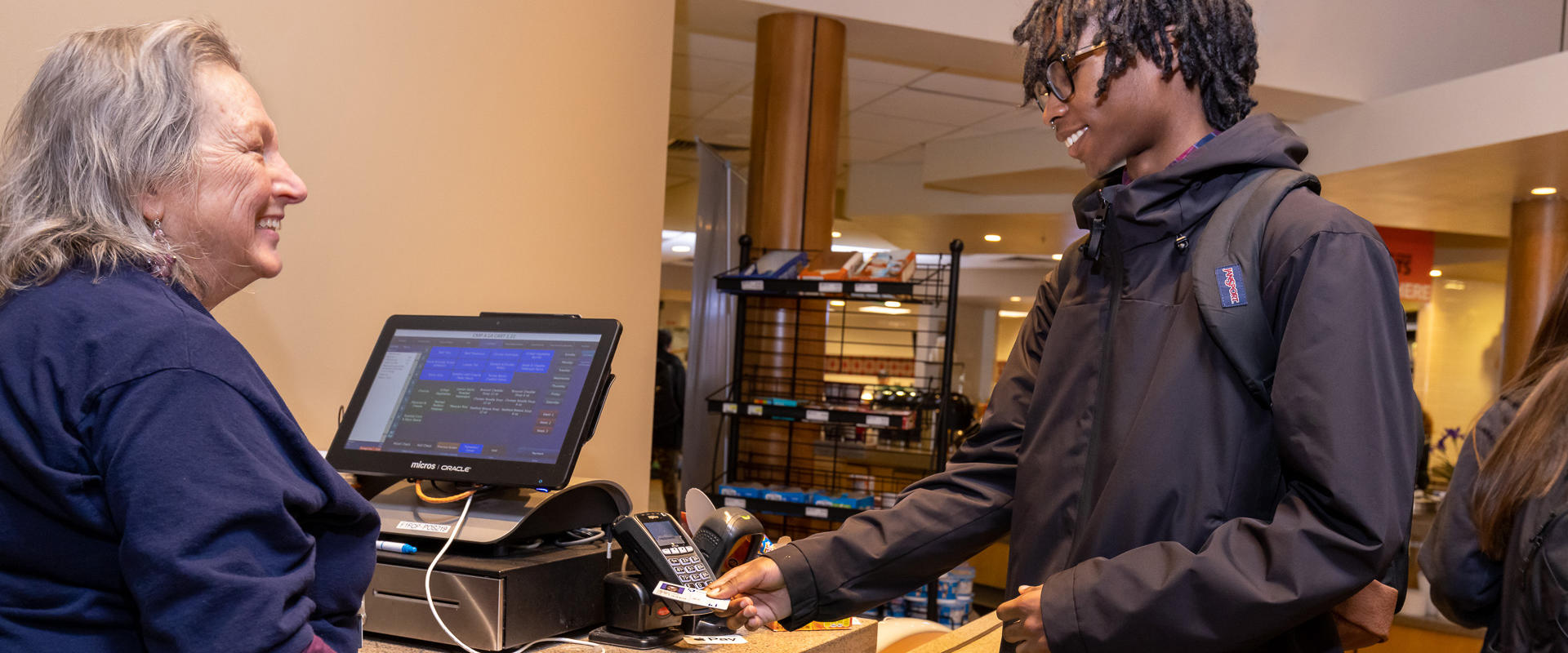 A student is swiping their meal card at a cashier station in the food court