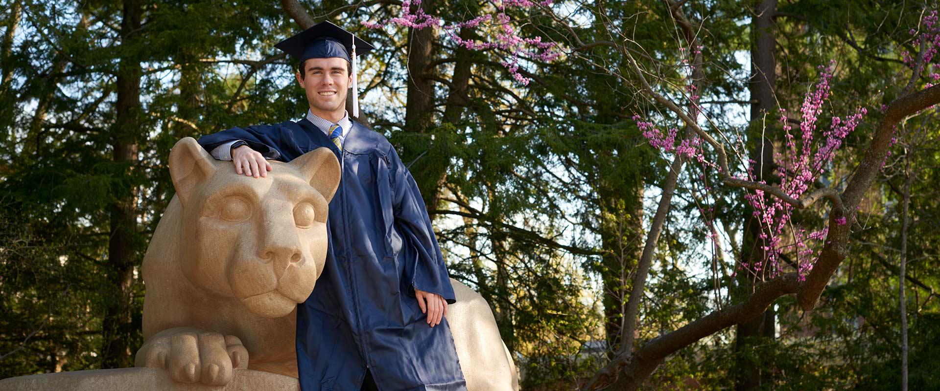 graduate poses with the Nittany Lion shrine