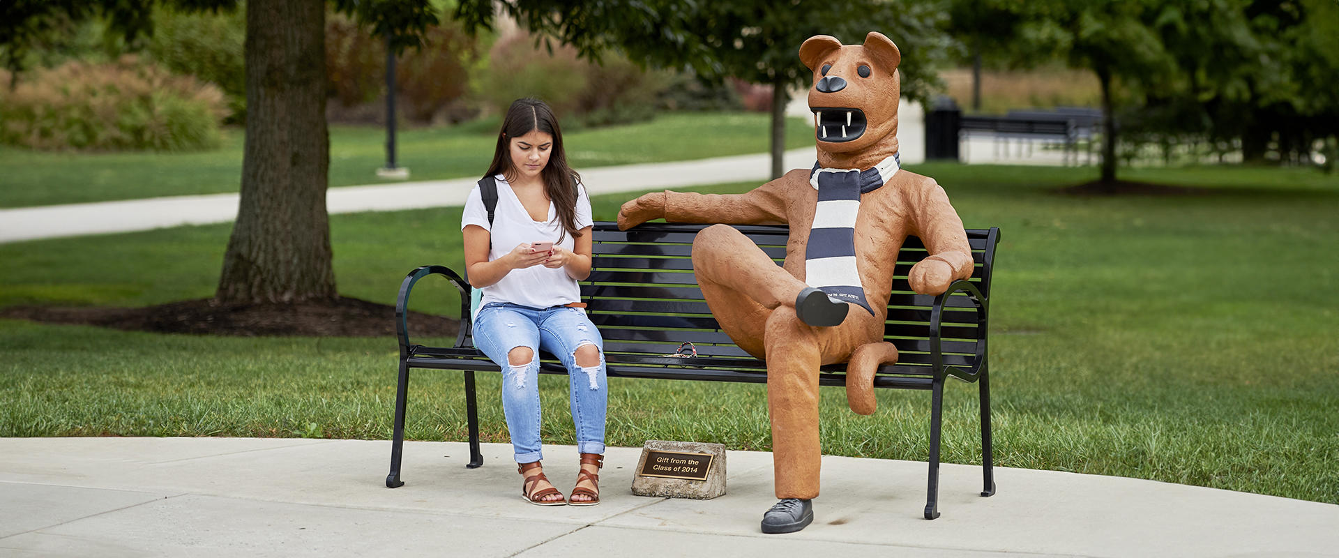 Student sits on bench next to Nittany Lion mascot