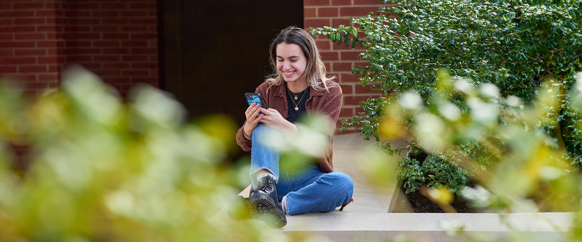 Student seated outside her residence hall using her phone